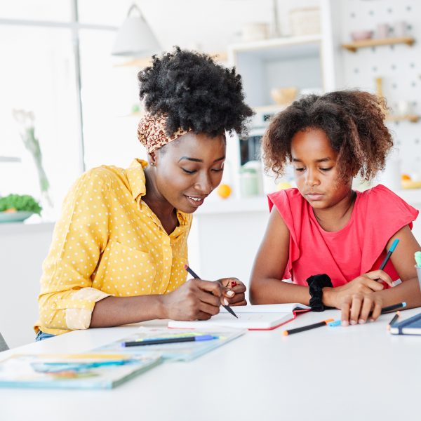 Happy mother teaching daughter and helping with homework at home